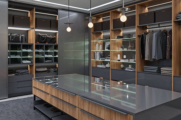 Closet planejado com iluminação embutida, ilha central e portas de vidro